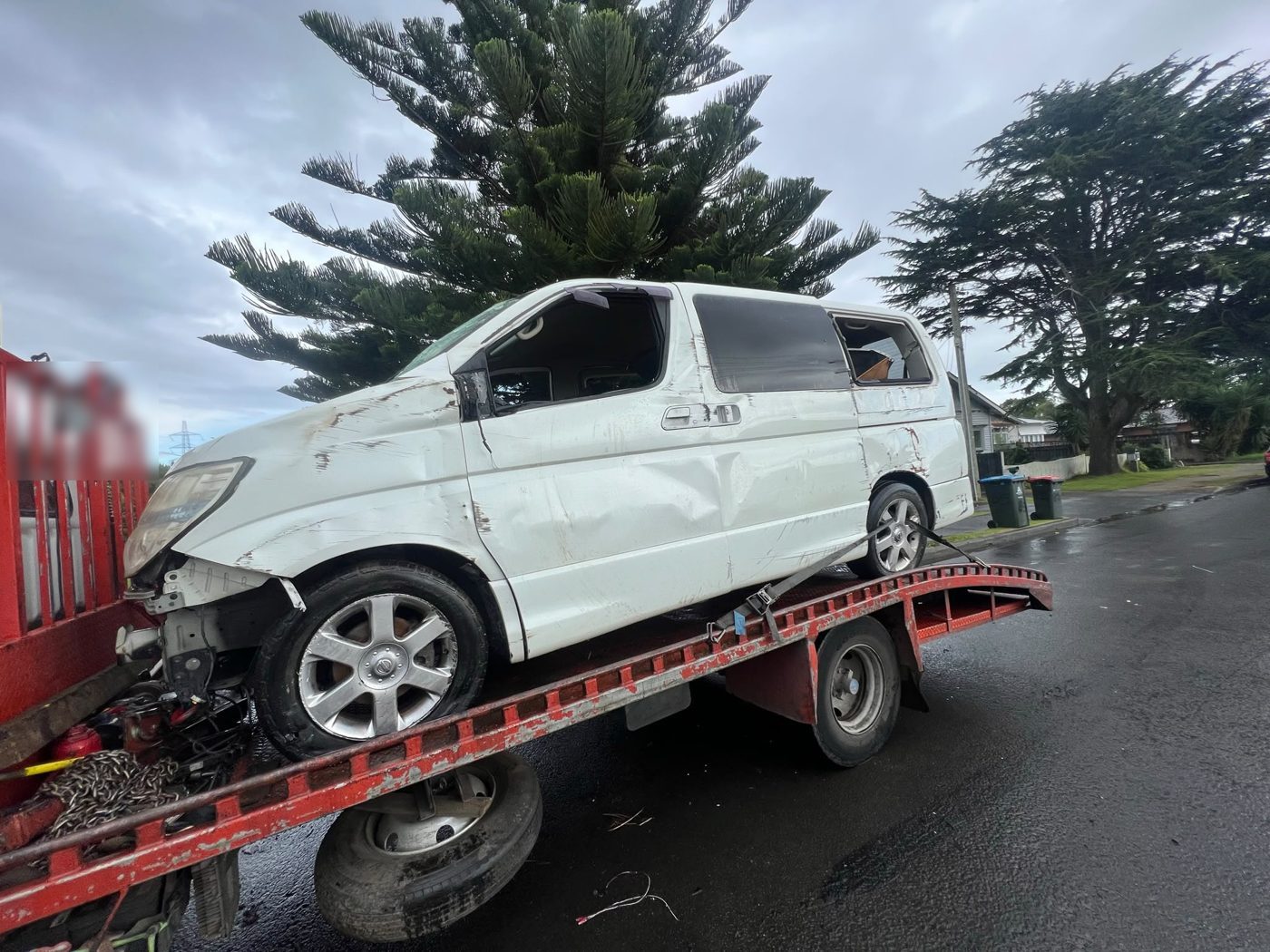 Damaged Nissan Elgrand van loaded on a tilt-tray tow truck in Auckland