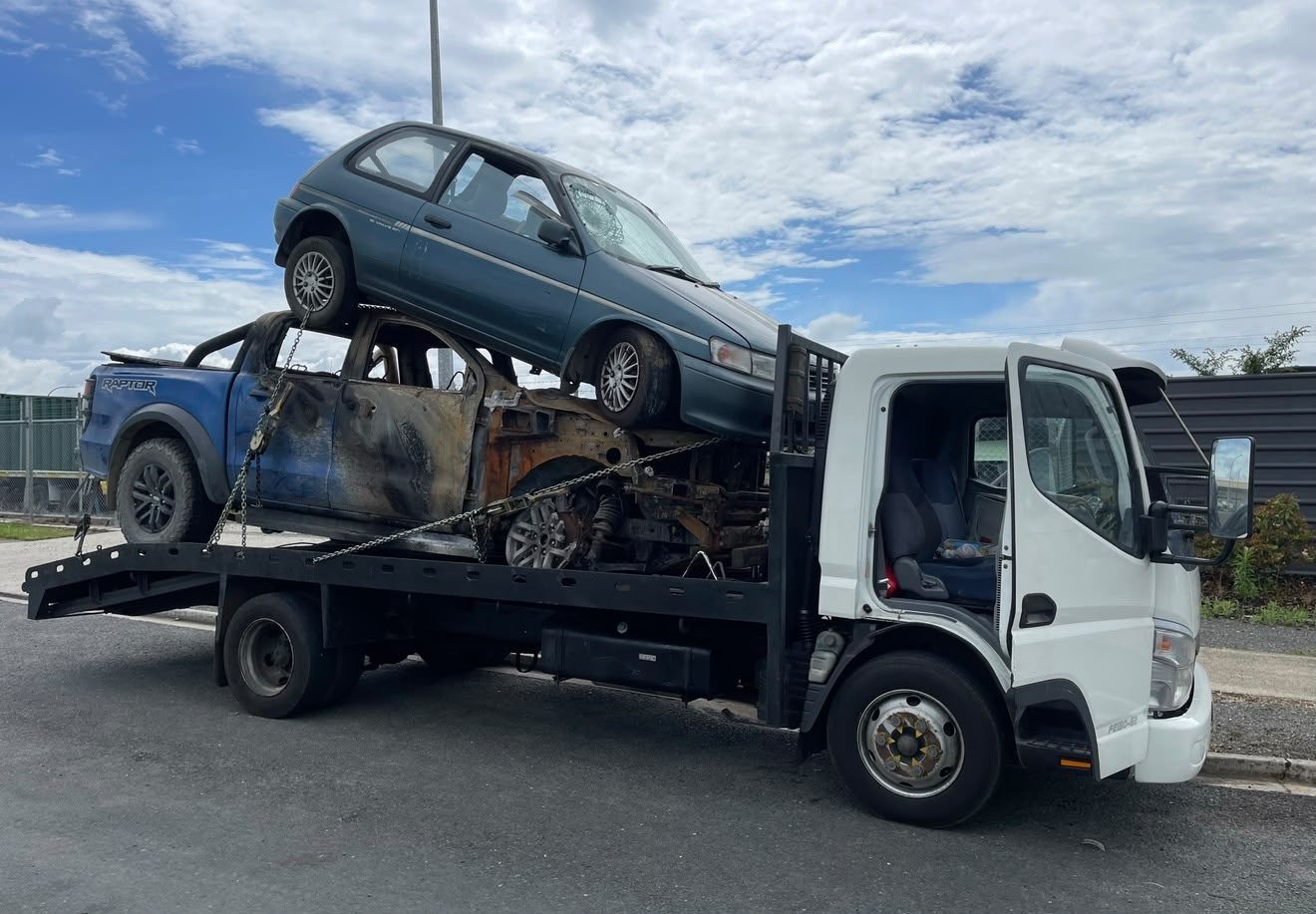 Burnt-out ute and a scrap hatchback loaded on a flatbed truck in Auckland