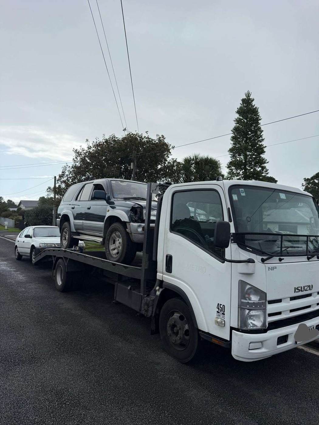 Isuzu tow truck carrying a 4WD and towing a car on an Auckland street